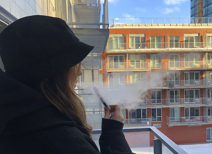 Girl vapes flavoured e-liquid outside an apartment building in Montreal Quebec