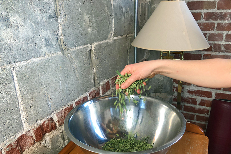 A person putting herbs into a metal bowl
