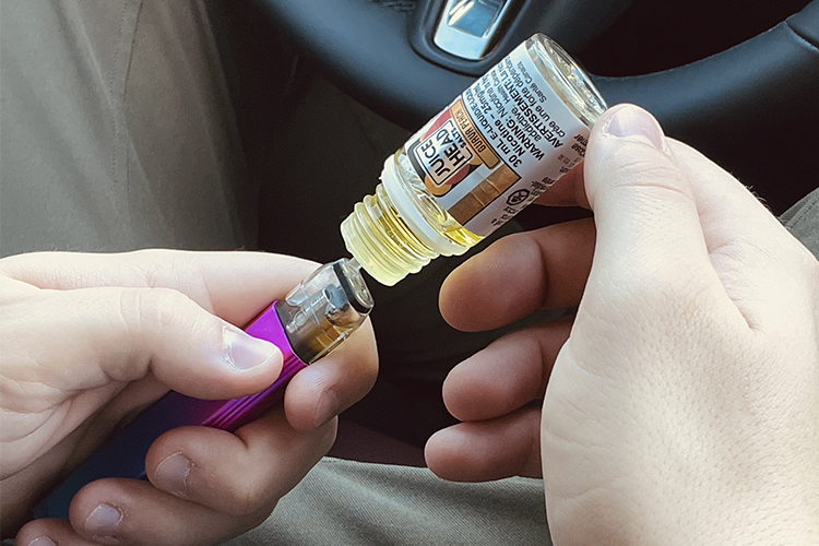 Hands pouring vape e-liquid into a vaporizer