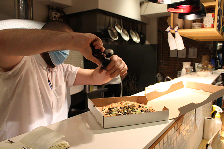 Chef grinds pepper onto a pizza for delivery