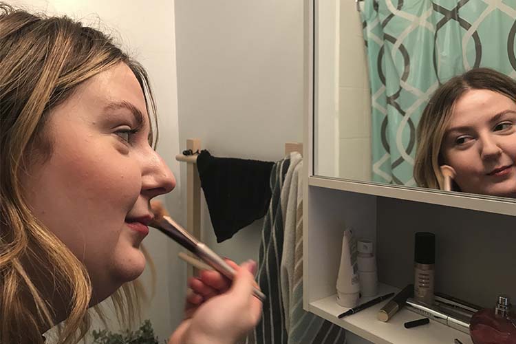 A woman applies makeup from an online beauty business looking into the mirror