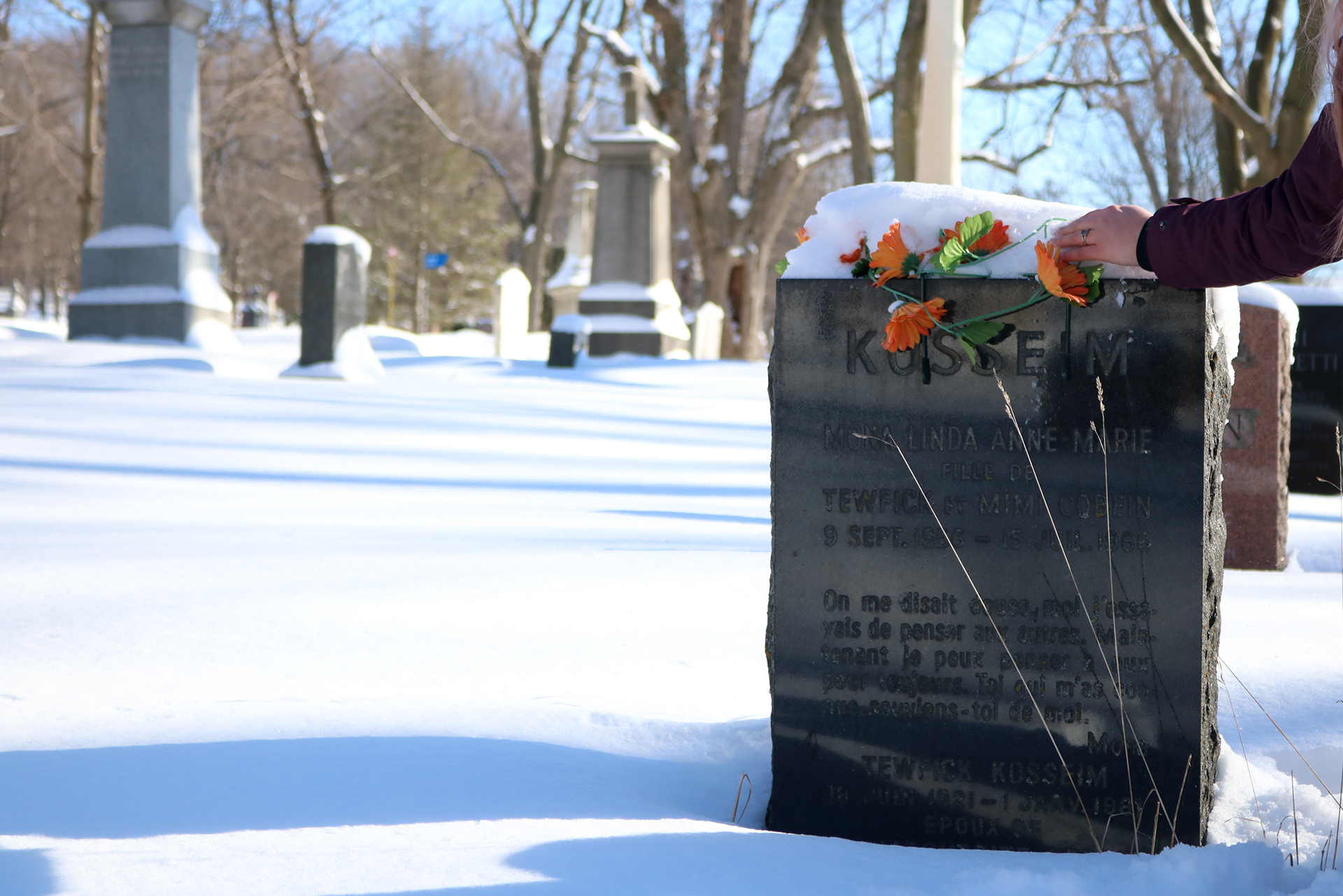 Person touches gravestone with orange flowers.