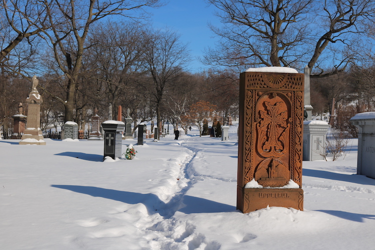 Gravestones in Notre Dame de Neiges Cemetery, a walking path in the center of the image guiding the eye to the forest backdrop