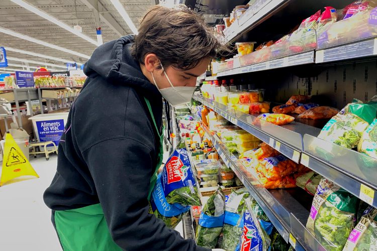 Man stocking grocery shelves with bags of spinach.