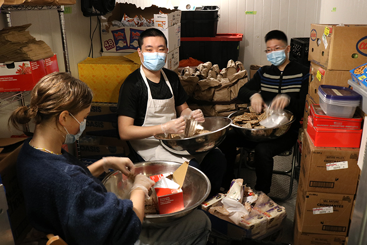 Three volunteers preparing snacks in a small room