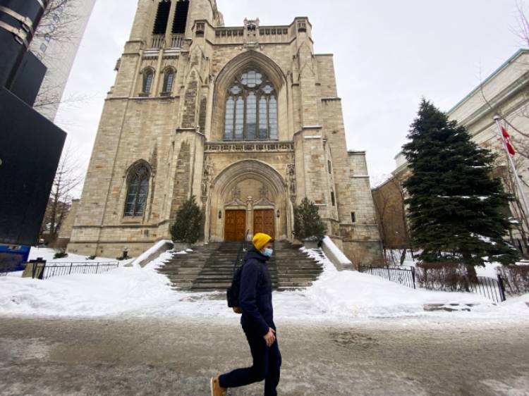 Person wearing yellow beanie walks in front of church's facade during the winter