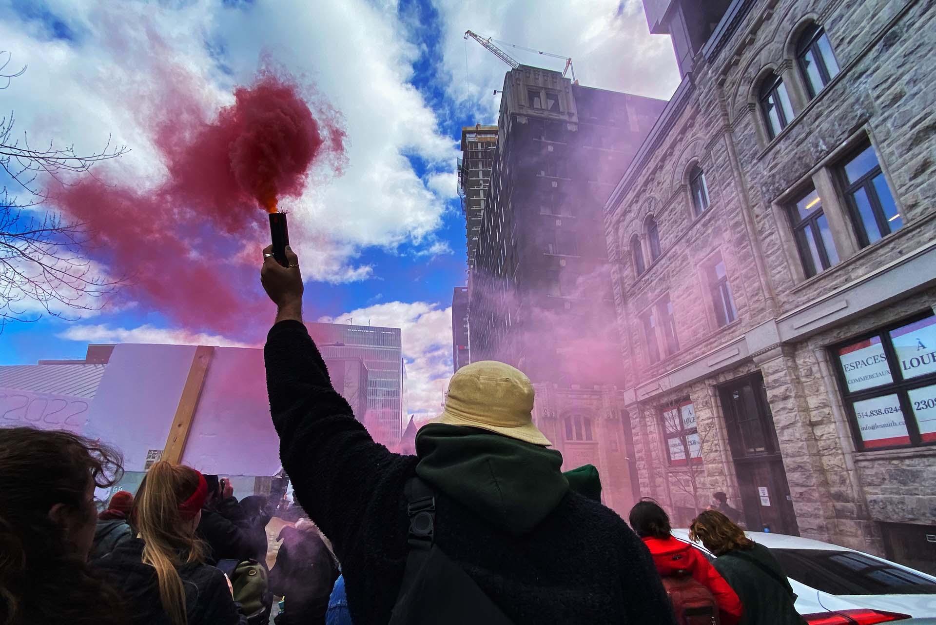 A man in a demonstration holds a smoke bomb. Red smoke comes out of it.