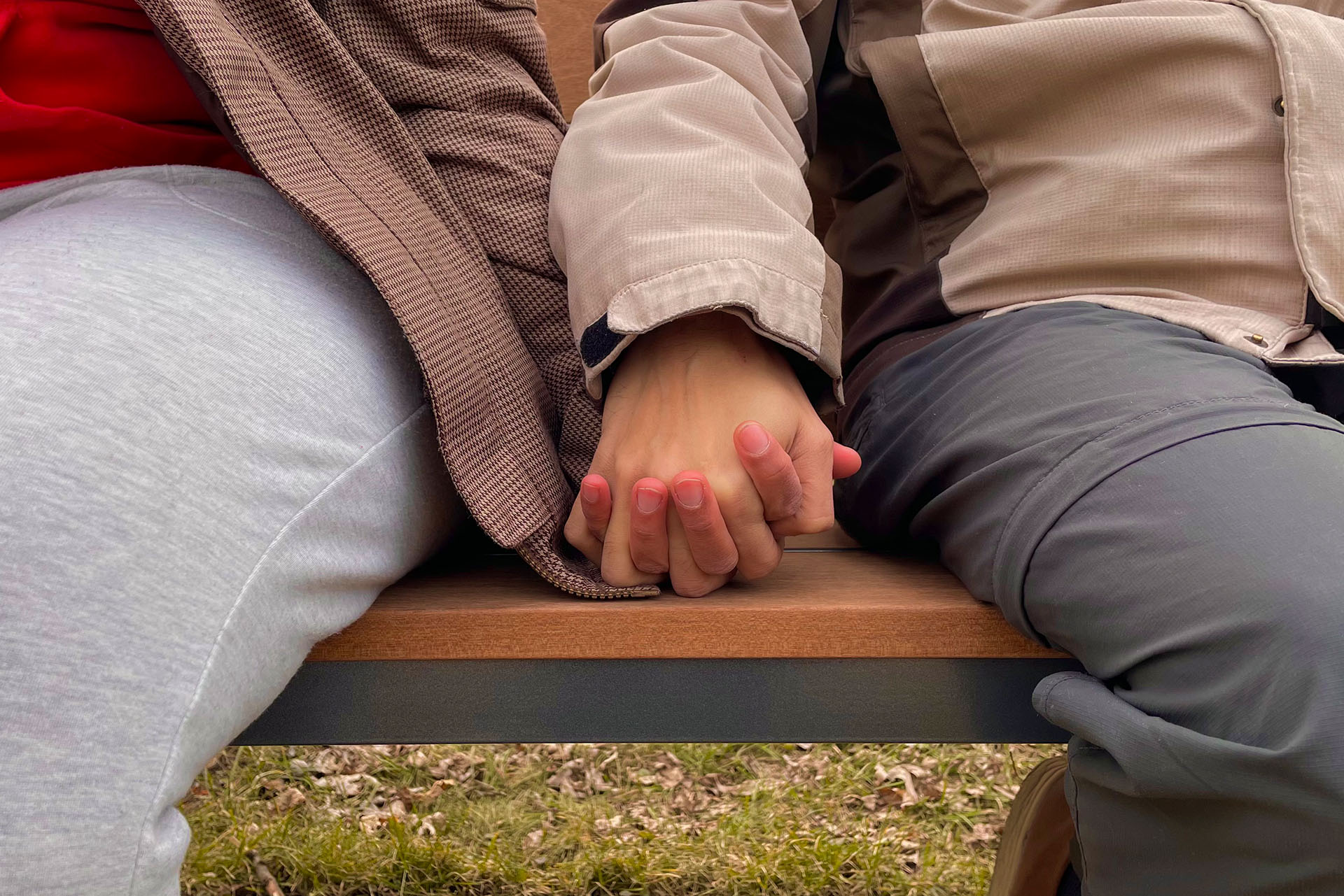 A close-up image of the hands of a couple sitting on a bench.
