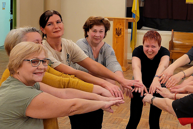 Movement therapist smiles while dancing with multiple women putting hands together in a circle.