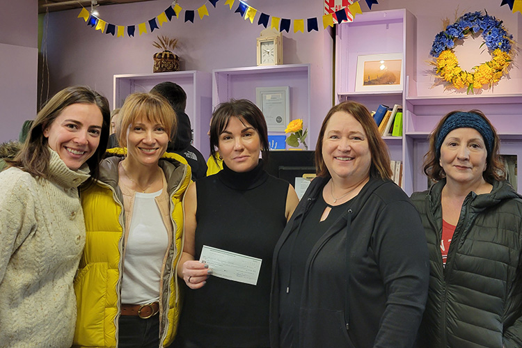 Five women smile together while holding a cheque at the donations hub.