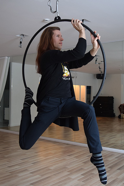 A woman sits on a hula hoop that is secured to the ceiling.