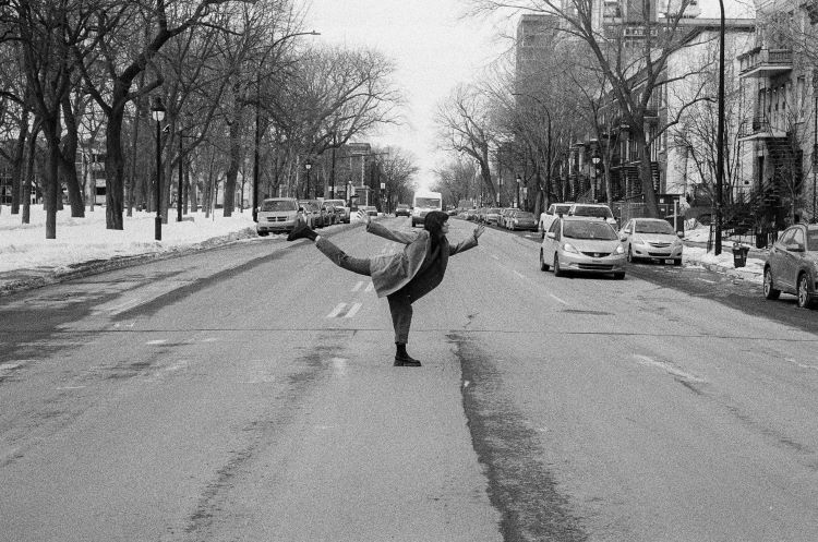 Woman dancing in the middle of a street, cars can be seen in the background.