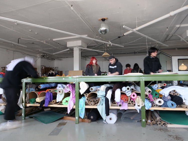 People stand around a workshop table full of fabric.