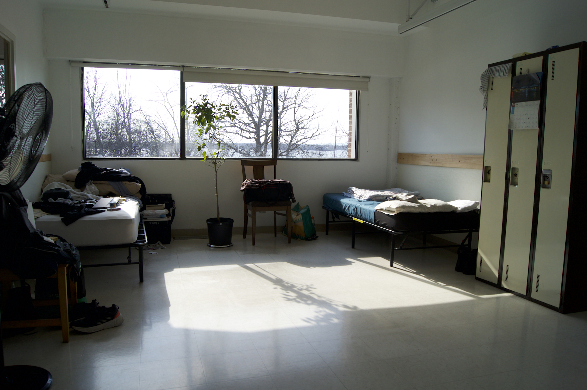 A room with two single beds on opposing walls with the sun shining between the two of them