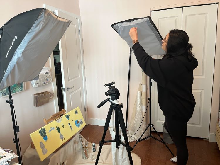 An artist setting up lighting and camera equipment around one of her paintings