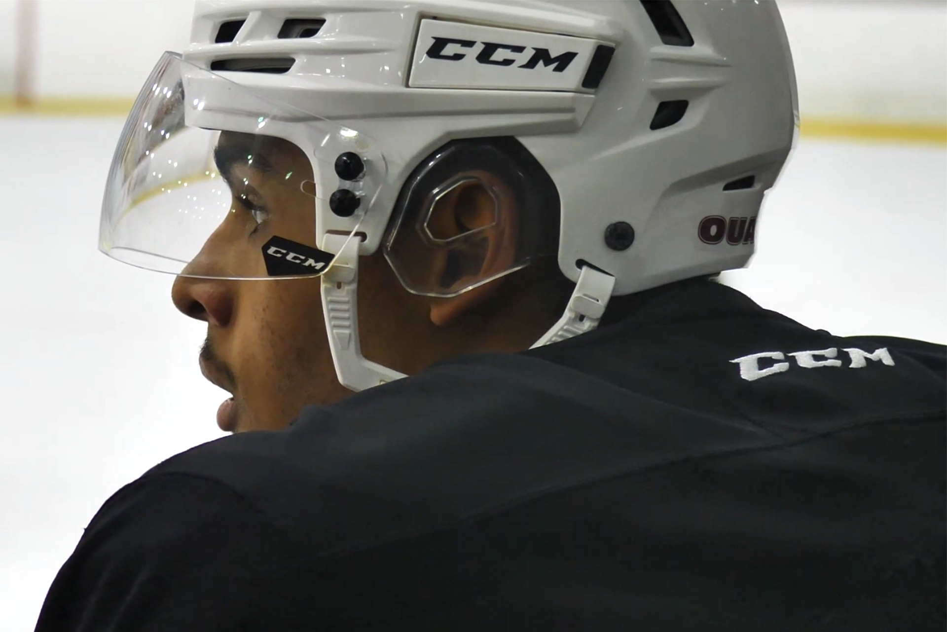 Hockey player Isiah Campbell watching his teammates from the bench during practice