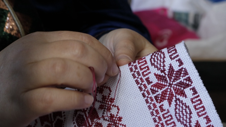 A close-up to a woman stiching with a red thread