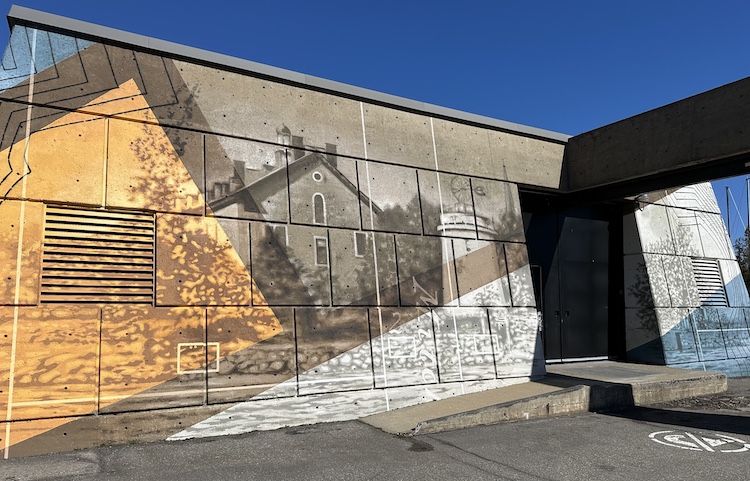 A mural depicting a house is painted along the side of a pumping station.